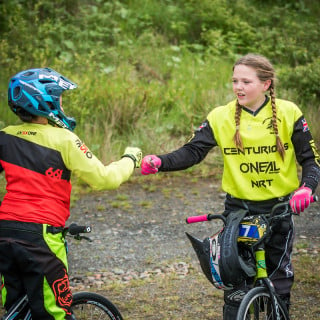 Two girls in BMX kit, standing over BMX bikes, bumping fists