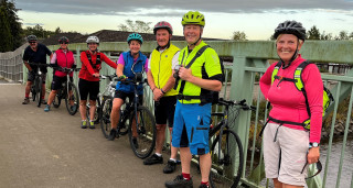 Four female and three male cyclists standing with their bikes on a bridge