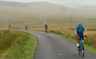 Four cyclists riding on a single-track road, in amongst rolling hills